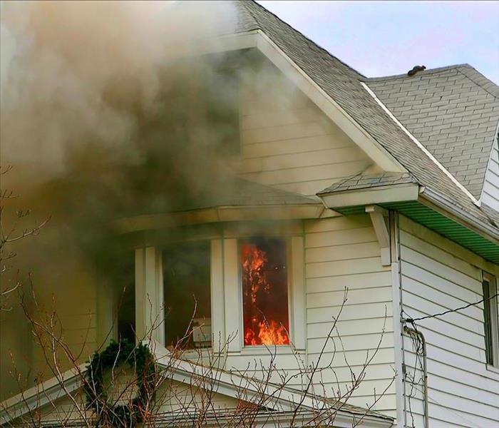 Smoke coming out of the second story of a white house. Fire can be seen in the window.